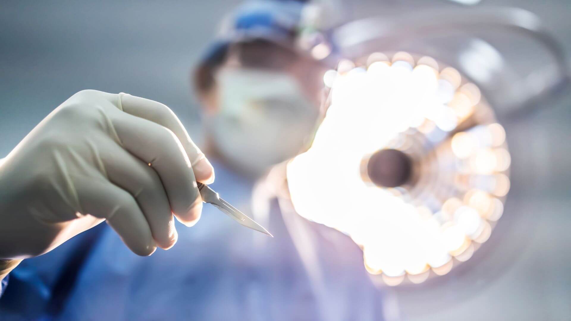 Ein chirurgischer Facharzt steht in einem OP-Saal und hält ein Skalpell in der Hand