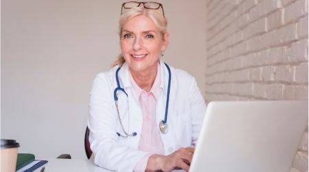 shutterstock.com/Gyorgy Barna Eine Oberärztin sitzt während ihrer Arbeit mit einem Laptop am Schreibtisch